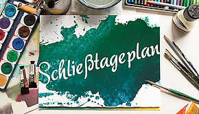 Das Bild zeigt einen Arebeitstisch. Darauf stehen Malkasten und verschiedene Pinsel. In der Mitte ist eien Bild, dass scheinbar mit diesen Bildern gemalt worden ist. Darauf steht in weißer Schrift "Schließtageplan". Das restliche Blatt ist in grün und türkis Tönen gemalt.