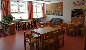 Es wird ein Gruppenraum gezeigt mit Tischen und Stühlen. Im Hintergrund befinden sich die Fenster