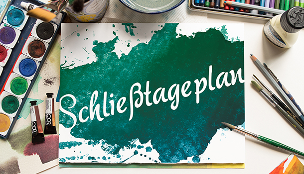 Das Bild zeigt einen Arebeitstisch. Darauf stehen Malkasten und verschiedene Pinsel. In der Mitte ist eien Bild, dass scheinbar mit diesen Bildern gemalt worden ist. Darauf steht in weißer Schrift "Schließtageplan". Das restliche Blatt ist in grün und türkis Tönen gemalt.